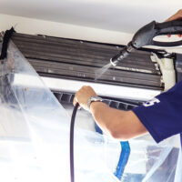 The technicians are cleaning the air conditioner by spraying water. Hand and water spray are cleaning the air conditioner on white background.